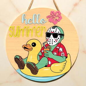 以下が含まれることがあります： 「hello summer」の文字が青と黄色で書かれた丸い木製の看板。ホッケーマスク、サングラス、アロハシャツを着た漫画のキャラクターが、黄色の浮き輪アヒルでくつろいでいます。ピンクの花が右上隅にあります。