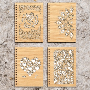May include: Set of four wooden notebooks with laser cut designs. The designs include a rose, a mandala, a heart made of smaller hearts, and a floral pattern with roses.
