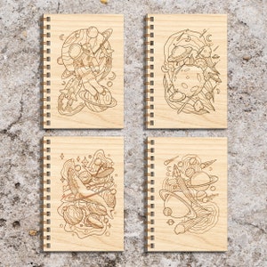 May include: Set of four wooden spiral notebooks with a space theme. Each notebook features a different design with planets, stars, and a rocket ship or whale.