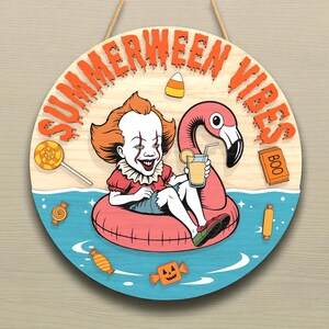 Könnte beinhalten: Rundes Holzschild mit den Worten "SUMMERWEEN VIBES" in Orange. Das Schild zeigt einen Cartoon-Clown in einem Flamingo-Schwimmer, der ein Getränk hält. Süßigkeiten und das Wort "BOO" sind ebenfalls abgebildet.