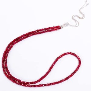 May include: A necklace featuring multiple strands of small, faceted, deep red beads. The necklace has a silver-colored clasp and chain, and the beads are strung together to create a layered effect. The background is plain white.