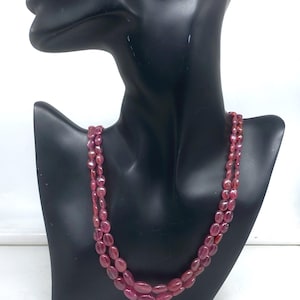 Puede incluir: Un collar de dos hilos compuesto por piedras preciosas ovaladas de color rojo intenso. El collar se exhibe en un maniquí negro, mostrando el color y el diseño de la joya. Las piedras tienen un acabado pulido.