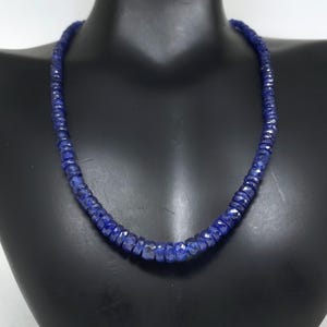 Può includere: Collana di pietre preziose blu scuro sfaccettate, esposta su un manichino nero. La collana è composta da numerose piccole perle di dimensioni uniformi, creando un filo continuo ed elegante. Le perle hanno una forma leggermente irregolare.