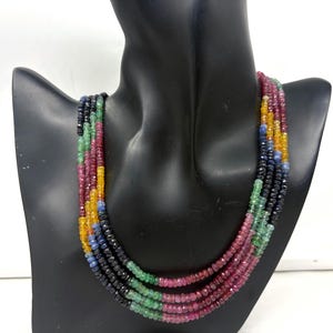 Peut inclure: Un collier à plusieurs rangs orné de pierres précieuses colorées. Le collier présente un dégradé de couleurs, notamment le bleu, le vert, le rouge, le jaune et le noir. Les perles, petites et rondes, sont enfilées pour créer un effet de superposition.