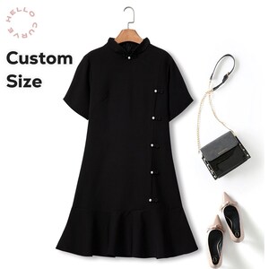 May include: A black short-sleeved dress with a button-up front and a ruffled hem. The dress has a collar and is styled with a black purse and nude heels.