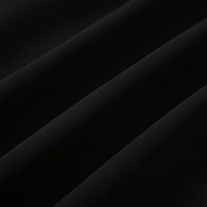 May include: Close-up of a black fabric with a smooth, soft texture. The fabric is folded and draped, creating a subtle wave pattern.