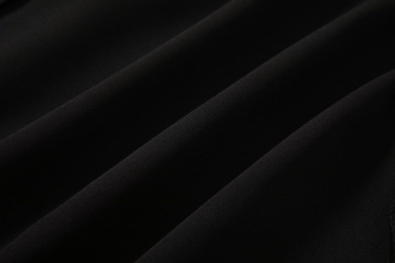 May include: Close-up of a black fabric with a smooth, soft texture. The fabric is folded and draped, creating a subtle wave pattern.