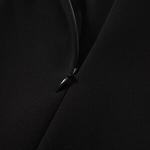 May include: Close-up of a black zipper on a garment. The zipper is partially open, revealing the black fabric underneath.