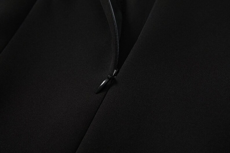 May include: Close-up of a black zipper on a garment. The zipper is partially open, revealing the black fabric underneath.