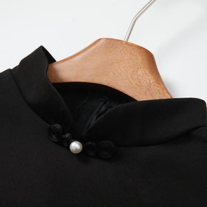 May include: Black mock neck top with a pearl button closure. The top has a mandarin collar.