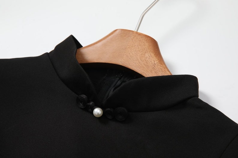 May include: Black mock neck top with a pearl button closure. The top has a mandarin collar.