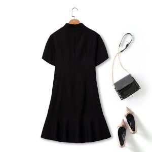May include: A black short-sleeved dress with a ruffled hem. The dress has a high neckline and a fitted bodice.