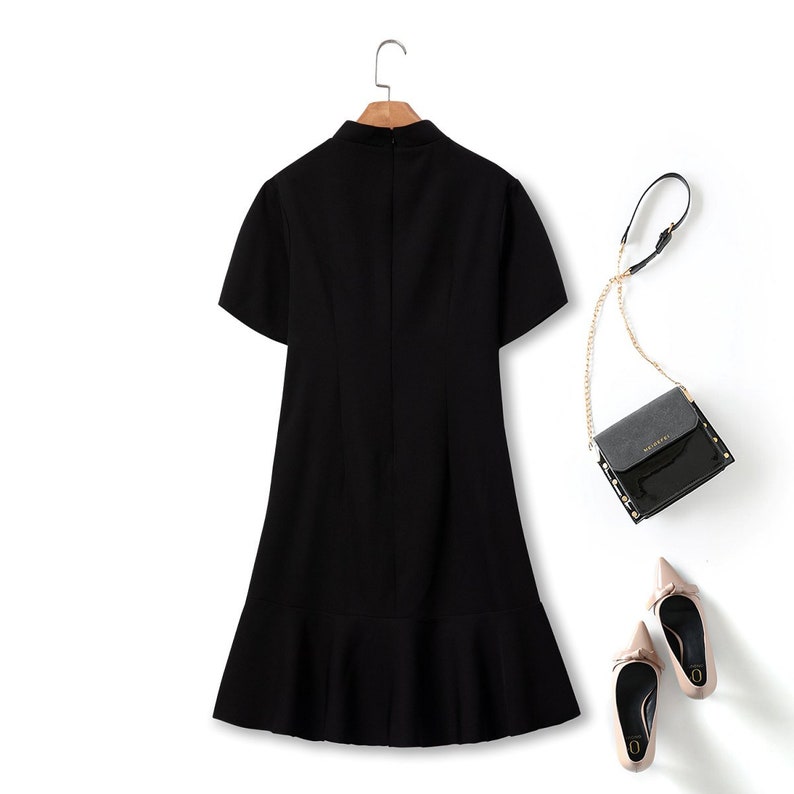 May include: A black short-sleeved dress with a ruffled hem. The dress has a high neckline and a fitted bodice.