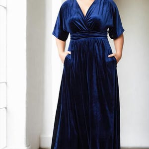 May include: A long, navy blue velvet maxi dress with a V-neckline and short sleeves. The dress has a fitted bodice and a flowing skirt.