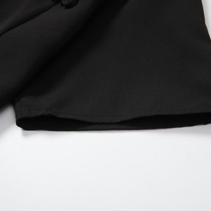 May include: Close-up of the black fabric sleeve of a dress with a pearl button detail.