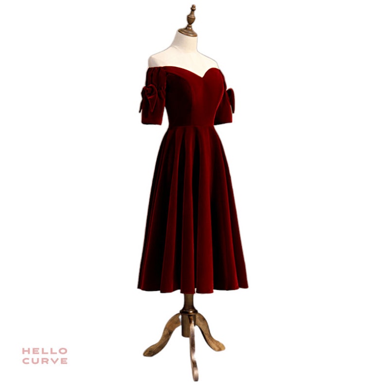 May include: A red velvet off-the-shoulder dress with short sleeves and a bow detail on each sleeve. The dress has a fitted bodice and a full skirt.