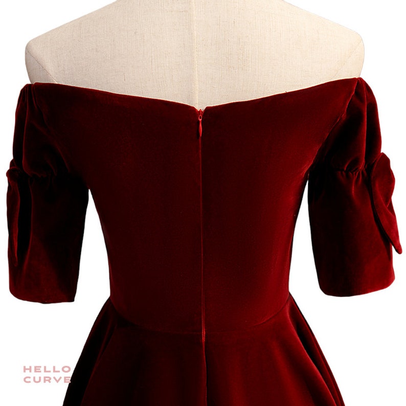 May include: Back view of a red velvet off-the-shoulder dress with short puff sleeves. The dress has a zipper closure in the back.