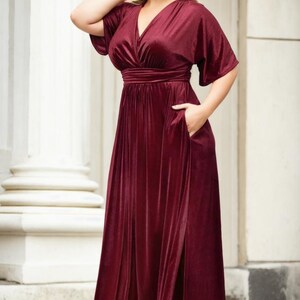 May include: A long, burgundy velvet maxi dress with a V-neckline, short sleeves, and a side slit. The dress has a fitted bodice and a flowing skirt.