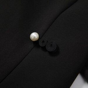 May include: A black fabric button with a pearl accent and a black fabric loop detail.