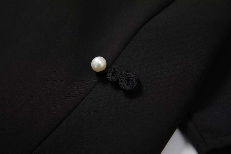 May include: A black fabric button with a pearl accent and a black fabric loop detail.