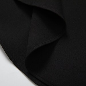 May include: Close-up of black fabric with a subtle texture. The fabric is folded and has a seam along the edge.