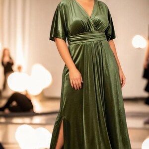 May include: A long, green velvet dress with a V-neckline and a wrap-style bodice. The dress has a side slit and short, wide sleeves.