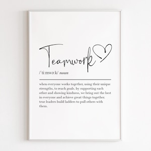 以下が含まれることがあります： 「Teamwork」の文字がスタイリッシュな筆記体で書かれたフレームプリント。ハートのシンボルが添えられています。チームワークの定義が下にあり、協力と相互支援を強調しています。