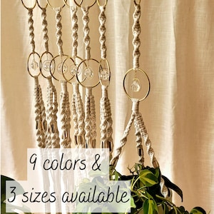 May include: Macramé plant hangers with gold rings and crystal accents. The hangers are in a neutral colour, with a woven design. The image includes text that says "9 colours & 3 sizes available."