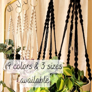 Peut inclure: Suspensions de plantes en macramé de différentes couleurs et tailles. L'image montre plusieurs suspensions de plantes en crème et noir, avec des plantes dans des pots blancs. Le texte de l'image indique "9 couleurs et 3 tailles disponibles."