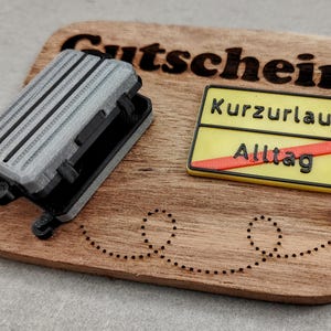 Könnte beinhalten: Ein Holz-Geschenkgutschein mit dem Wort "Gutschein" und einem kleinen Koffer sowie einem Schild mit der Aufschrift "Kurzurlaub" und "Alltag".