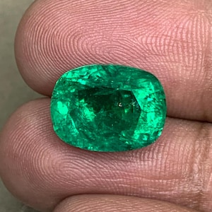 May include: A vibrant green emerald gemstone with a cushion cut. The emerald is set in a ring and has a polished finish.