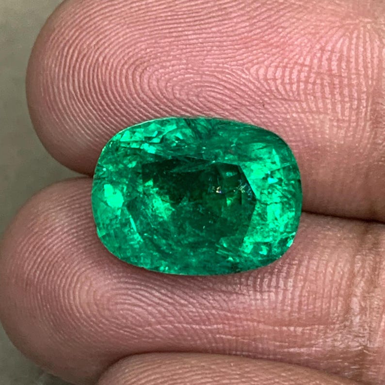 May include: A vibrant green emerald gemstone with a cushion cut. The emerald is set in a ring and has a polished finish.