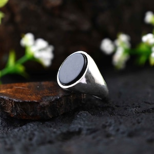 Op de afbeelding: Een zilveren ring met een zwarte ovale edelsteen. De ring ligt op een houten oppervlak.