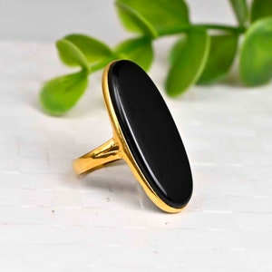 Puede incluir: Un anillo de oro con una gran piedra ovalada de ónix negro.