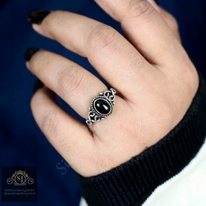May include: A silver ring with a black oval gemstone set in a decorative filigree design.