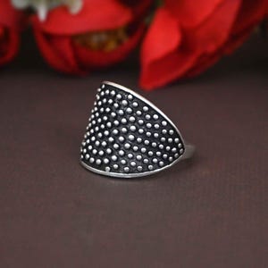 Puede incluir: Un anillo de plata con un diseño texturizado y punteado. El anillo tiene forma de triángulo y un acabado liso y pulido.