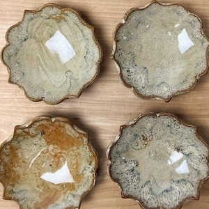 May include: Four handmade ceramic dishes with a unique scalloped edge. Each dish has a different glaze, including shades of beige, brown, and blue. The dishes are numbered 1 through 4.
