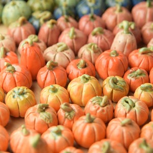 May include: A collection of miniature ceramic pumpkins in various colors, including orange, yellow, pink, green, and blue. Each pumpkin has a detailed stem and ribbed texture, perfect for fall decor.