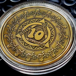 May include: A round bronze-colored recovery medallion encased in a clear plastic protective capsule. The coin features the number 10 in the center, surrounded by a triangle with the words Unity, Service, and Recovery, and a border of figures.