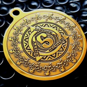 May include: A circular gold-toned medallion featuring a central number 5 surrounded by a triangle with the words SERVICE, UNITY, and RECOVERY. The outer border displays a repeating pattern of small figures in a circle, with a small loop at the top.