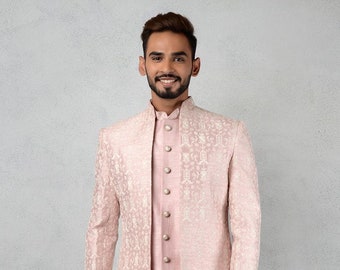 May include: A light pink, three-piece suit with a mandarin collar. The long jacket features a subtle, repeating pattern and is worn over a matching shirt and pants. The suit has a formal, elegant appearance.
