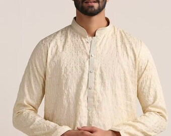 May include: A cream-coloured long-sleeved shirt with a mandarin collar and a button-up front. The shirt has a subtle embroidered pattern.