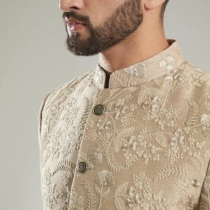 May include: A beige embroidered jacket with a mandarin collar and gold buttons. The jacket has a floral pattern.