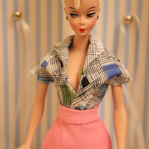 May include: A vintage doll with blonde hair styled in a high ponytail, wearing a black and white checked blouse with a pink skirt.
