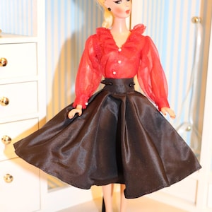May include: A vintage doll wearing a red sheer blouse with a ruffled collar and a black satin skirt. The doll has blonde hair and is wearing black shoes.