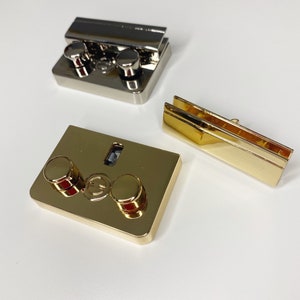 May include: Three gold-toned metal clasps with round, raised knobs. The clasps are designed for attaching to glass or other materials.