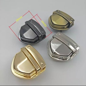May include: Three metal clasps in gold, silver, and black. Each clasp is shaped like a shield with a raised center and a hinged top. The clasps measure 42mm by 35mm.