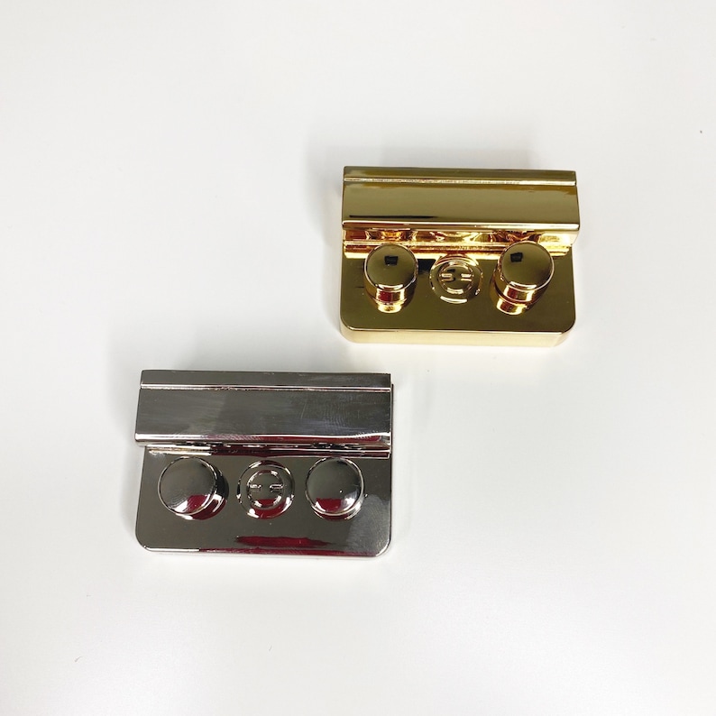 May include: Two metal clasps, one gold and one silver, with three round buttons each. The clasps are rectangular and have a raised edge.