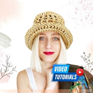 May include: A woman with blonde hair is wearing a gold crochet bucket hat. The hat has a wide brim and a woven design. The woman is looking at the camera and smiling. The text "VIDEO TUTORIALS" is displayed in blue with a play button icon.