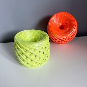May include: Two woven baskets, one is green and the other is orange. Both baskets are made of a woven material and have a round shape.